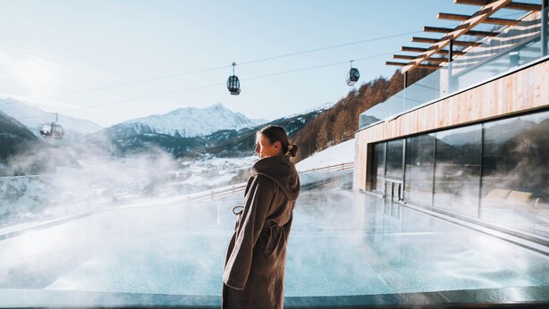 A person standing by a glass window overlooking a snowy mountain and a ski lift. - Grünwald Resort (Soelden)