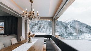 A modern dining area with a wooden table, a chandelier, and a view of snow-covered mountains. - Grünwald Resort (Soelden)