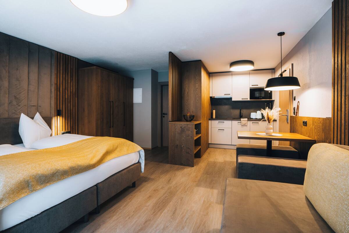 A modern hotel room with a large bed, a desk, and a kitchenette.
