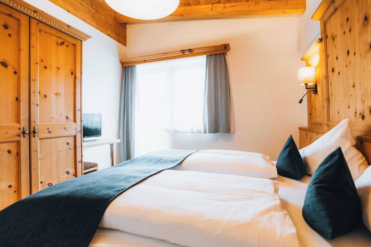 A bedroom with a large bed, wooden wardrobe, and a television on a small table.