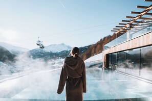 A person standing by a glass window overlooking a snowy mountain landscape with a ski lift in the distance.