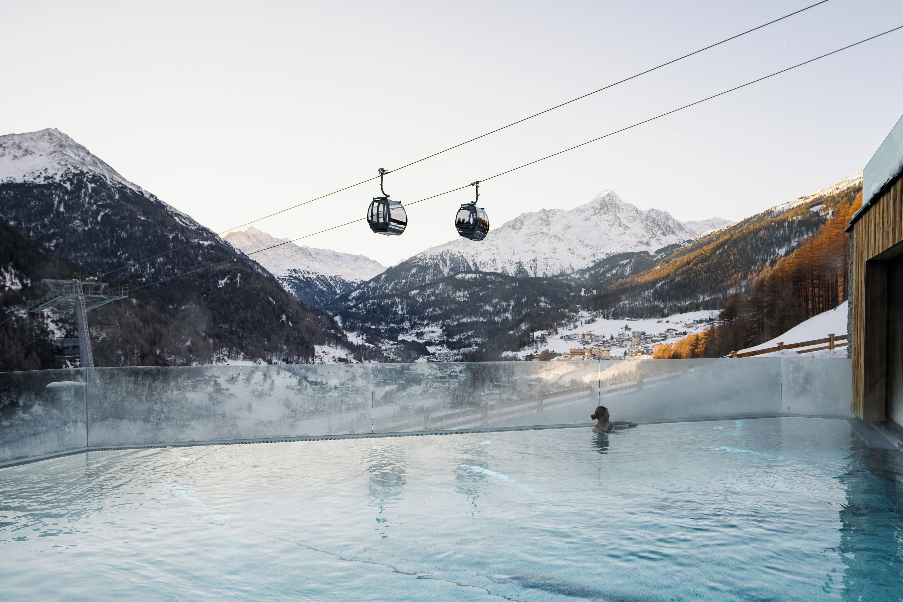 Un jacuzzi con vista a la montaña, dos teleféricos y un edificio de madera.