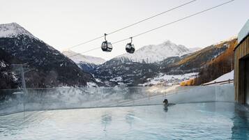 Un jacuzzi con vista a la montaña, dos teleféricos y un edificio de madera.