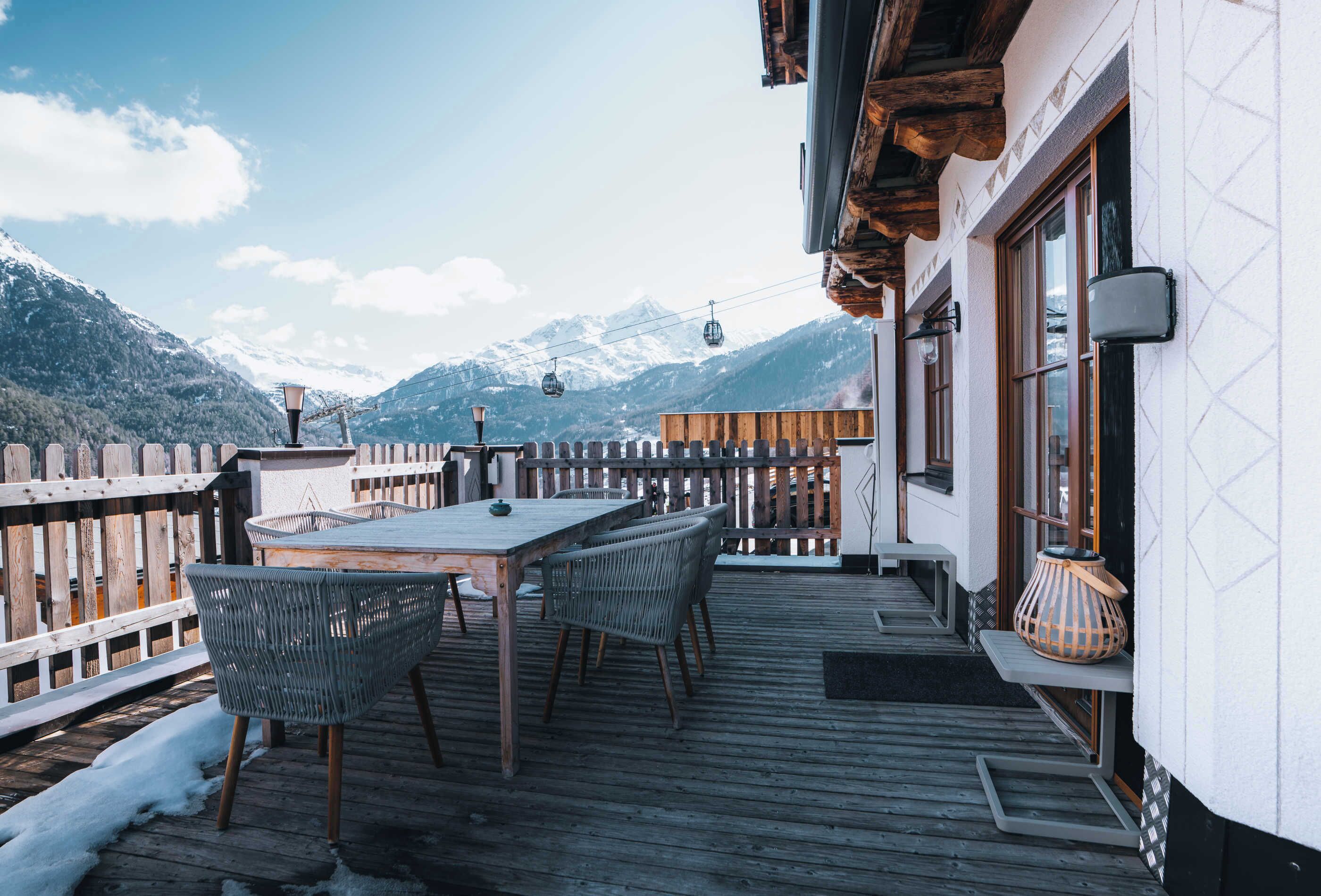A wooden deck with a table and chairs, overlooking a mountain range.