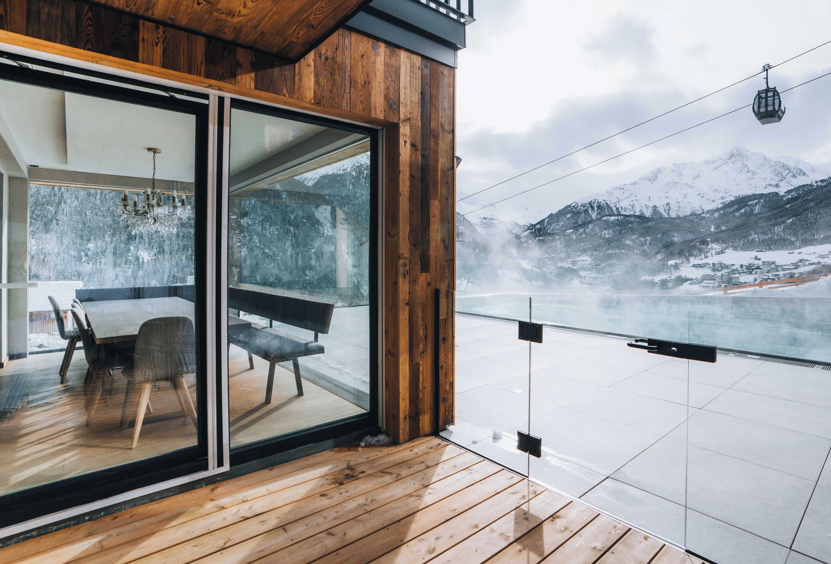 A modern wooden balcony with a glass door leading to a dining area with a table and chairs.