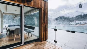 A modern wooden balcony with a glass door leading to a dining area with a table and chairs.