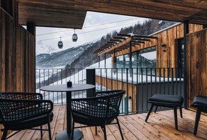 A wooden deck with a table and chairs, a glass balustrade, and a view of a snowy mountain landscape.