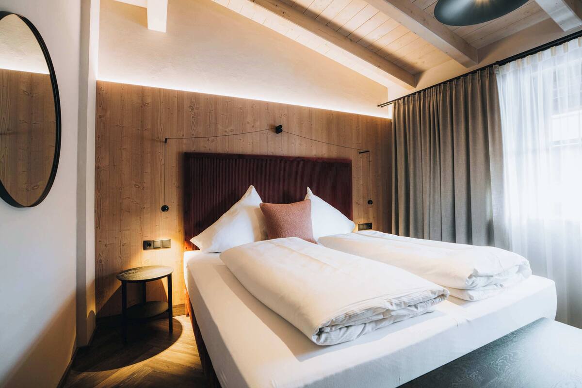 A modern hotel room with a wooden headboard, a small bedside table, and a large bed with neatly folded linens.