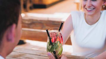 A person holding a drink with a straw and lime slice, sitting at a wooden table in a restaurant.
