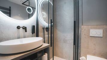 Un bagno moderno con uno specchio rotondo, un lavandino bianco e una cabina doccia in vetro.