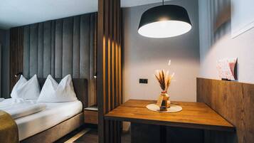 A modern hotel room with a bed, bedside table, and a dining area with a table and chair.