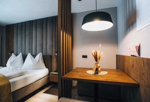 A modern hotel room with a bed, bedside table, and a dining area with a table and chair.