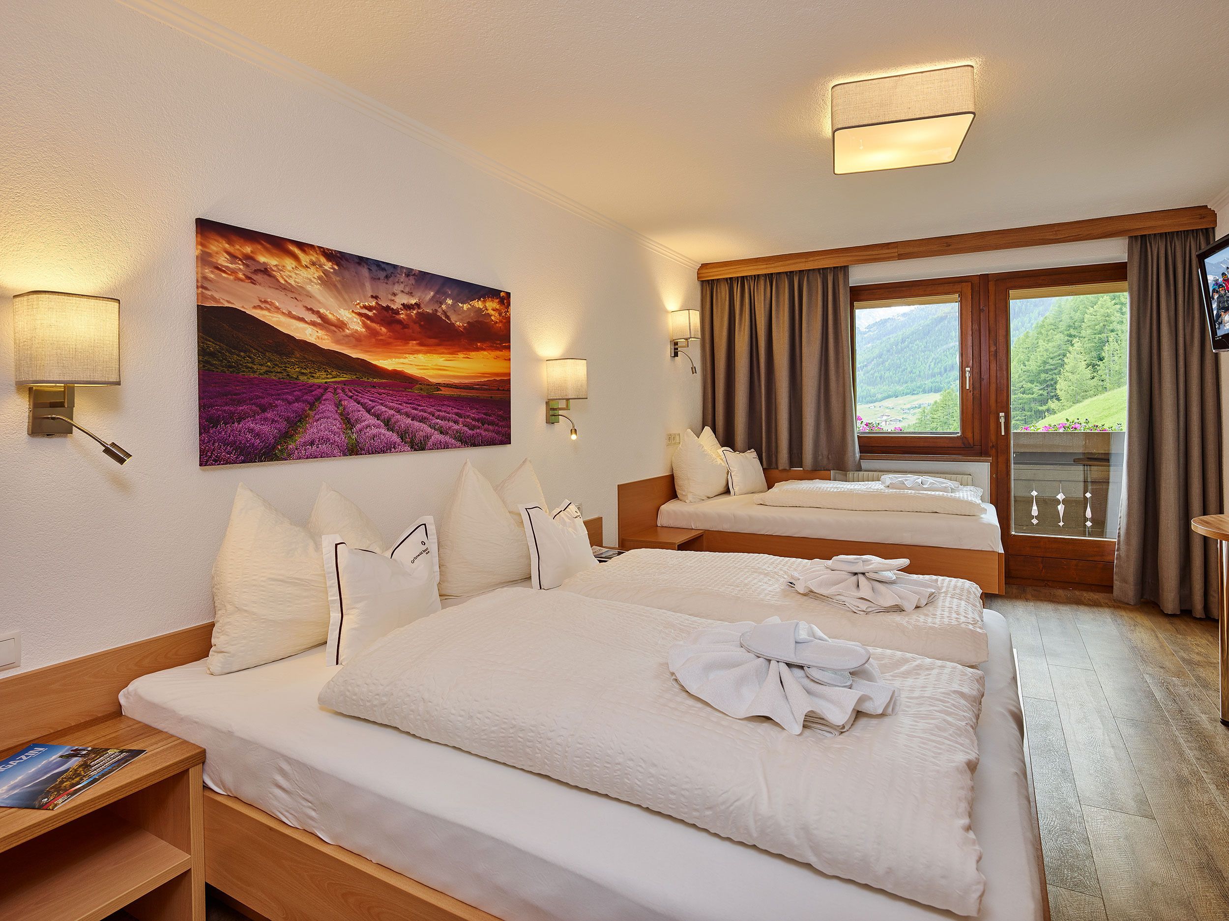 Ein Hotelzimmer mit zwei Betten, einem großen Fenster mit Blick auf ein Feld und einem Sonnenuntergangsbild.