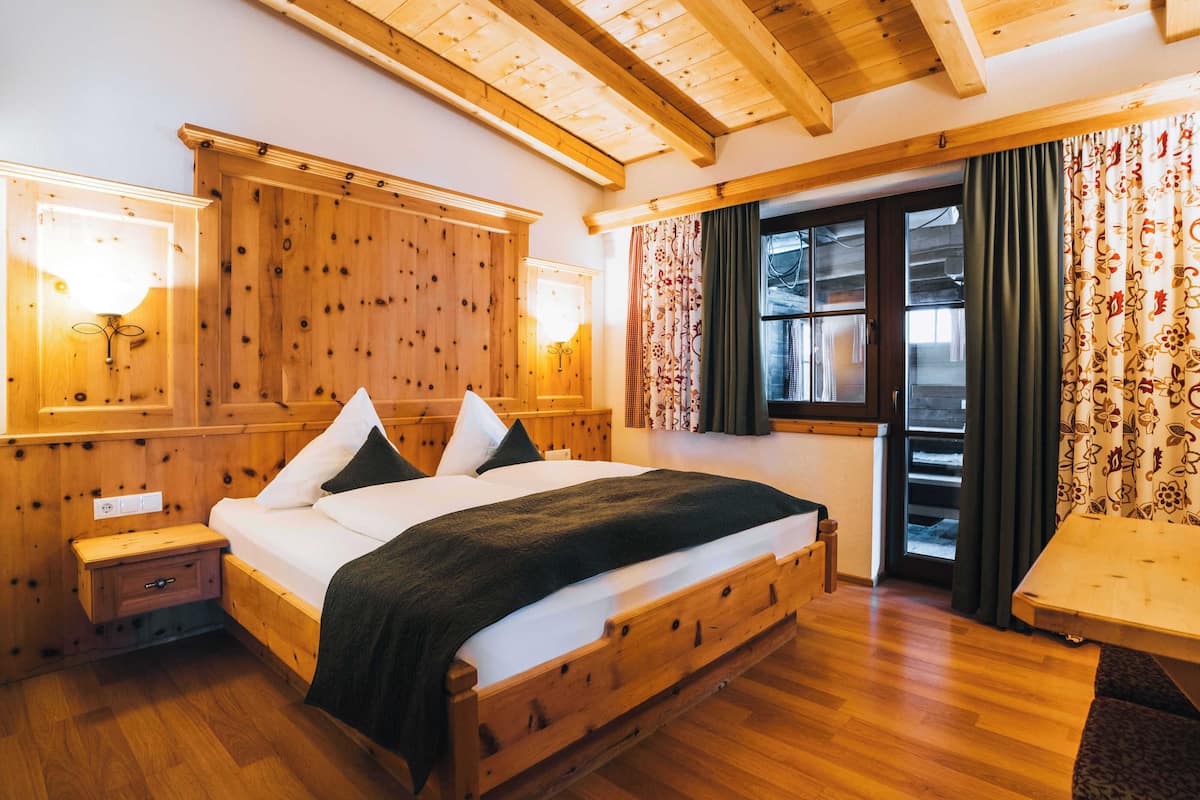 A wooden-framed bedroom with a large bed, wooden nightstands, and a window with curtains.