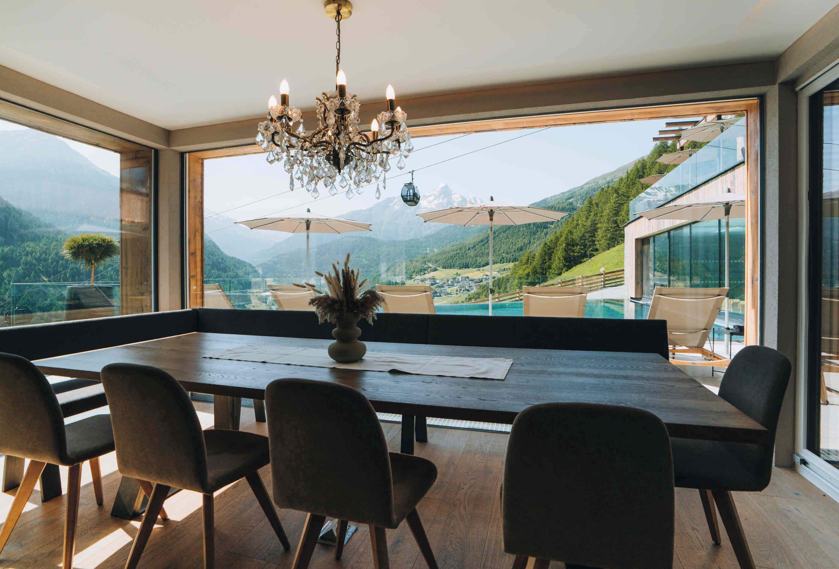 A dining area with a large table, chairs, and a chandelier. It features large windows with a mountain view.