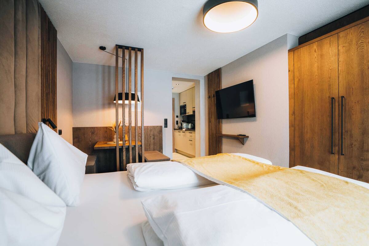 A modern hotel room with a bed, a desk, a TV, and wooden cabinets.