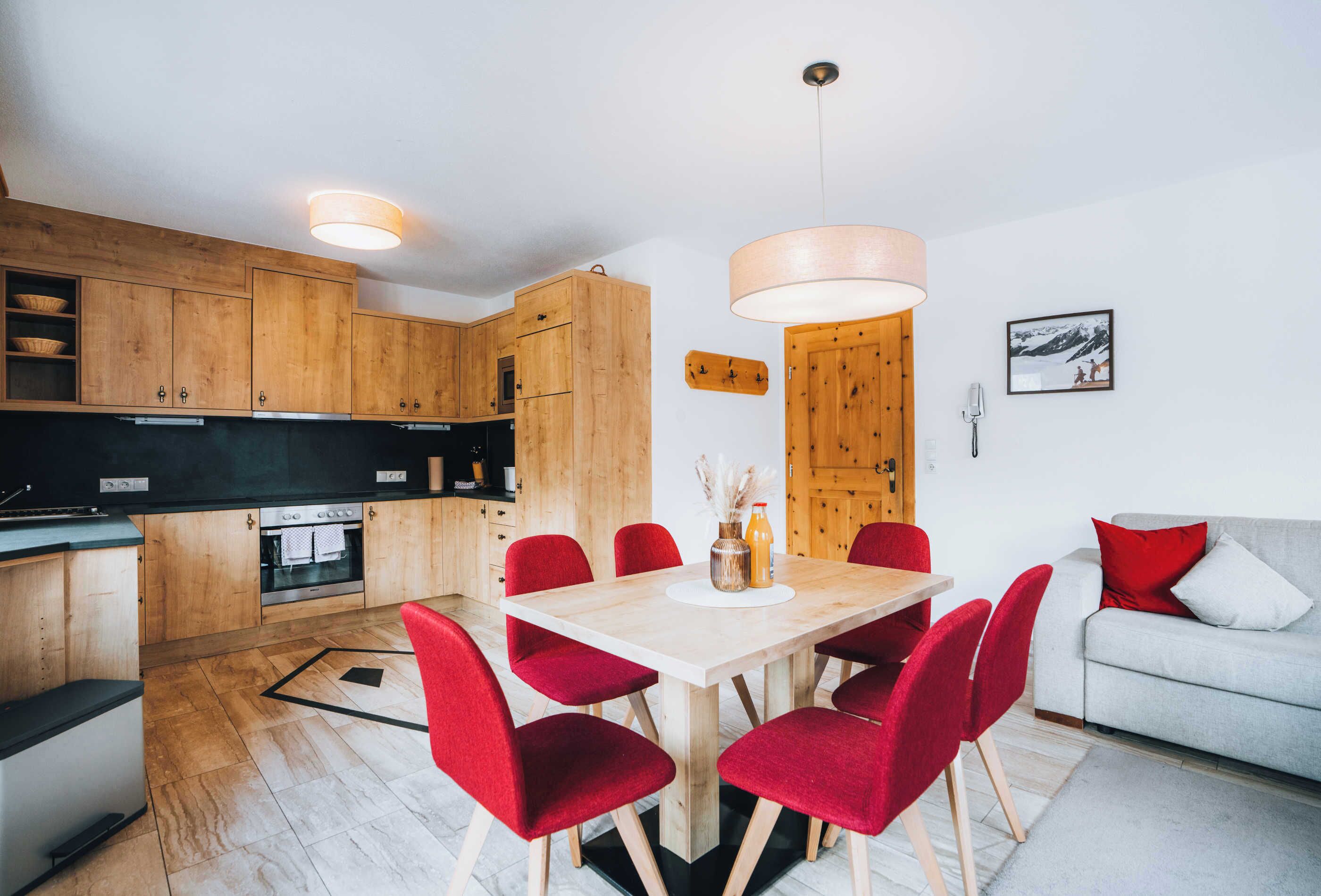 Une cuisine moderne avec des meubles en bois, une table à manger avec des chaises rouges et un canapé gris avec des coussins rouges.