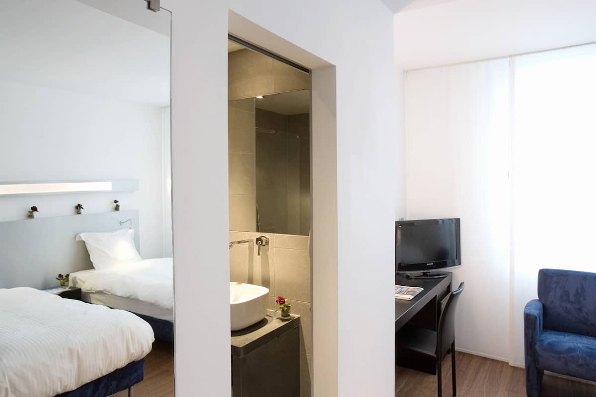 A hotel room with a bed, a desk with a TV, a bathroom with a sink, and a shower.