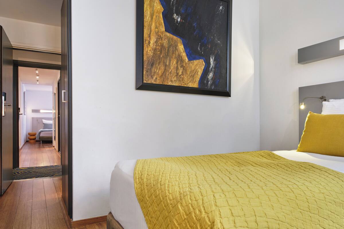 A hotel room with a bed, a painting on the wall, and a view into the bathroom.