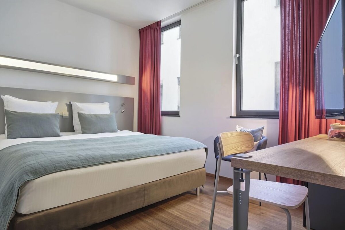 Een hotelkamer met een bed, een bureau en een raam met gordijnen.