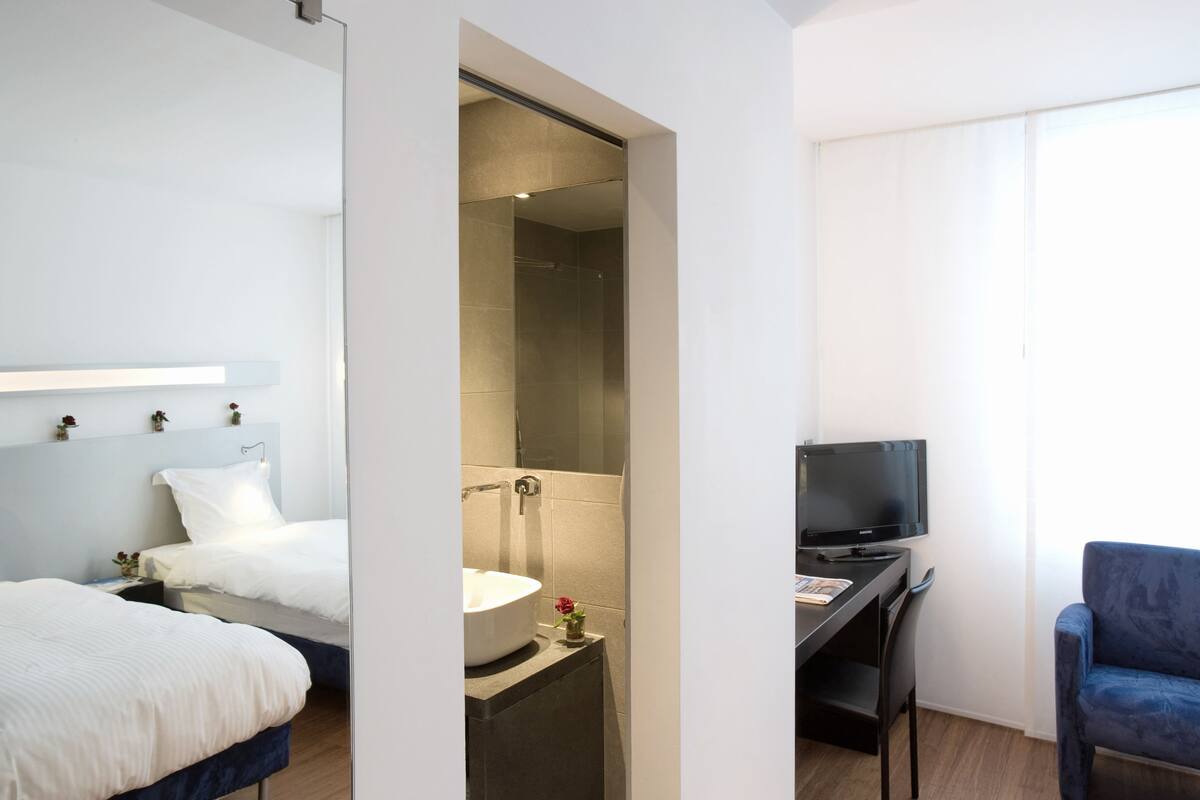 A hotel room with a bed, a desk with a TV, a bathroom with a sink, and a shower.