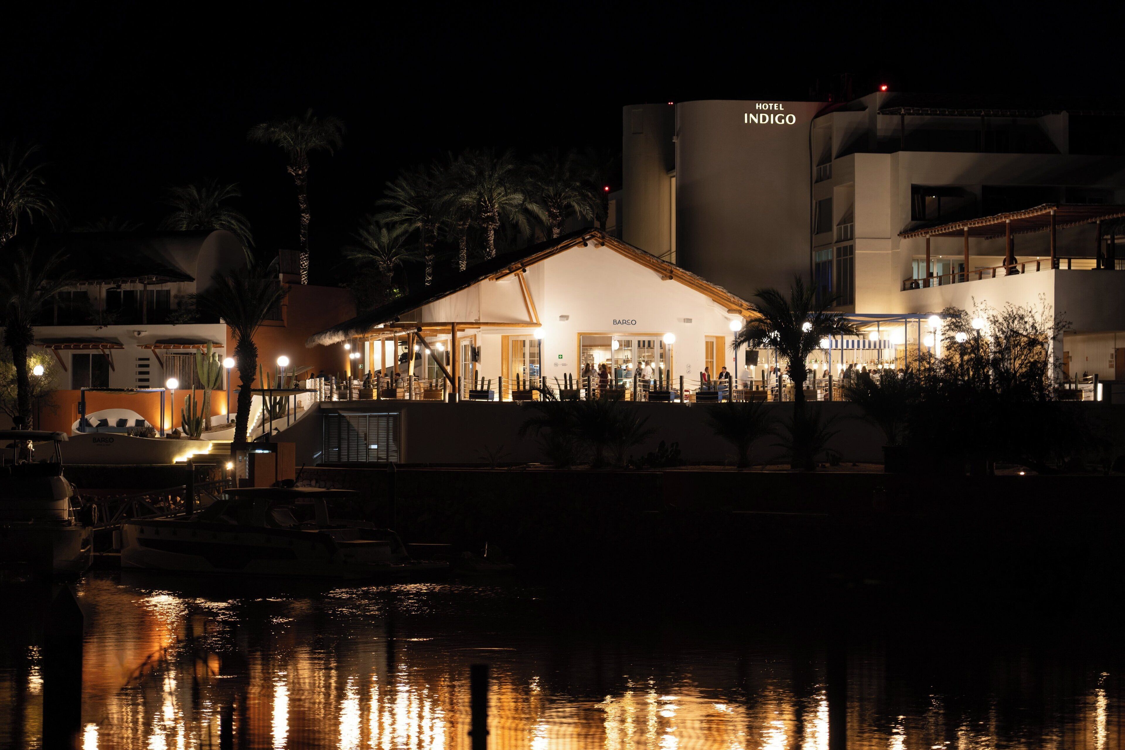 Un hotel frente al agua con fachada barroca, zona de piscina y barcos amarrados cerca.