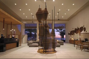 Un área de recepción moderna con una escultura de madera única, un mostrador de recepción, asientos y vistas al atardecer.
