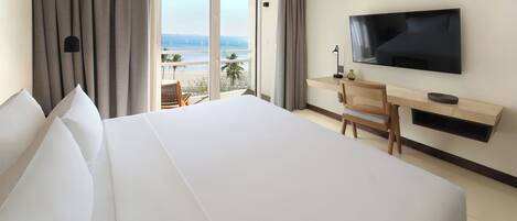 A hotel room with a large bed, a desk, a flat-screen TV, and a balcony with a view of the sea.