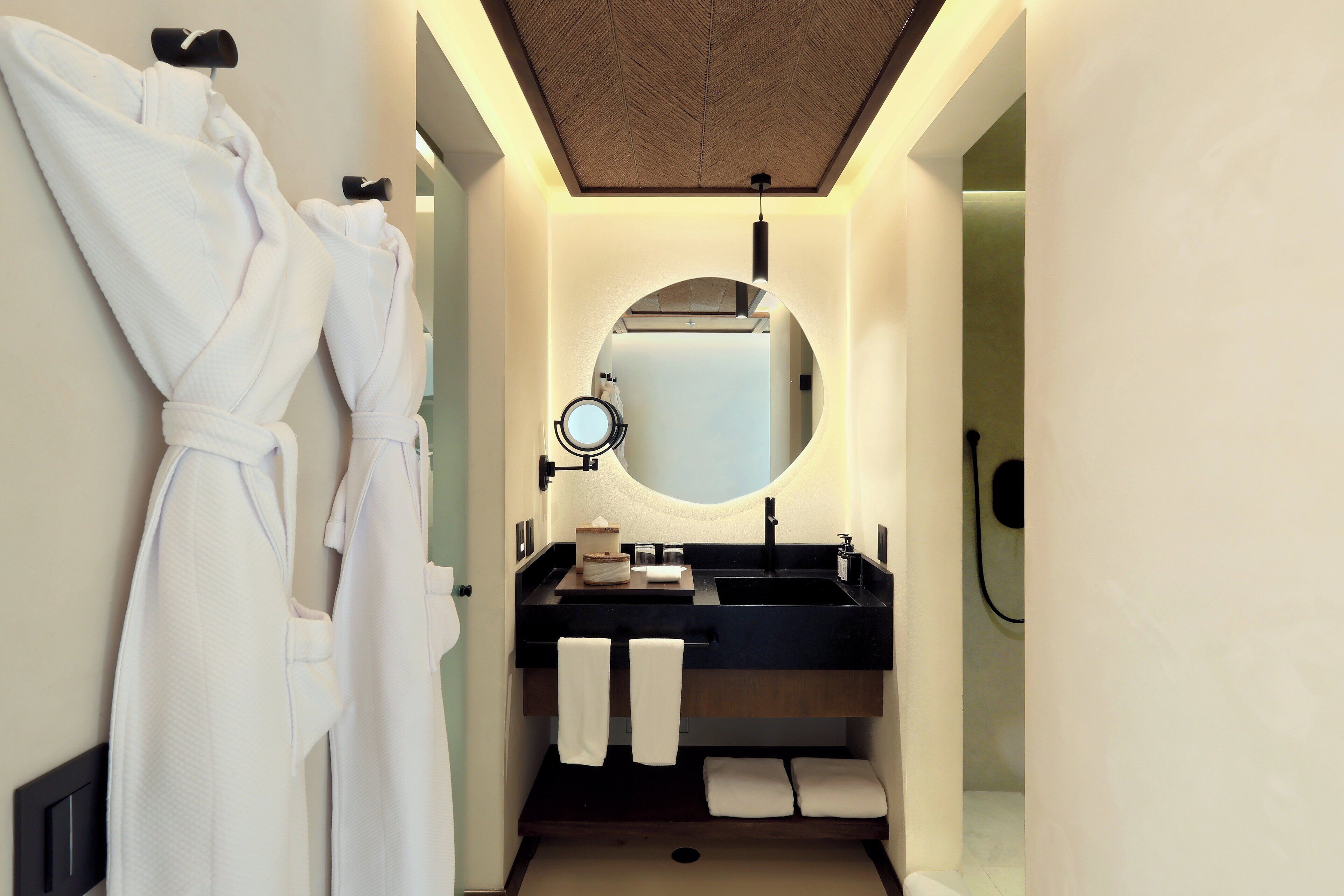 A modern bathroom with a round mirror, black sink, and white towels.