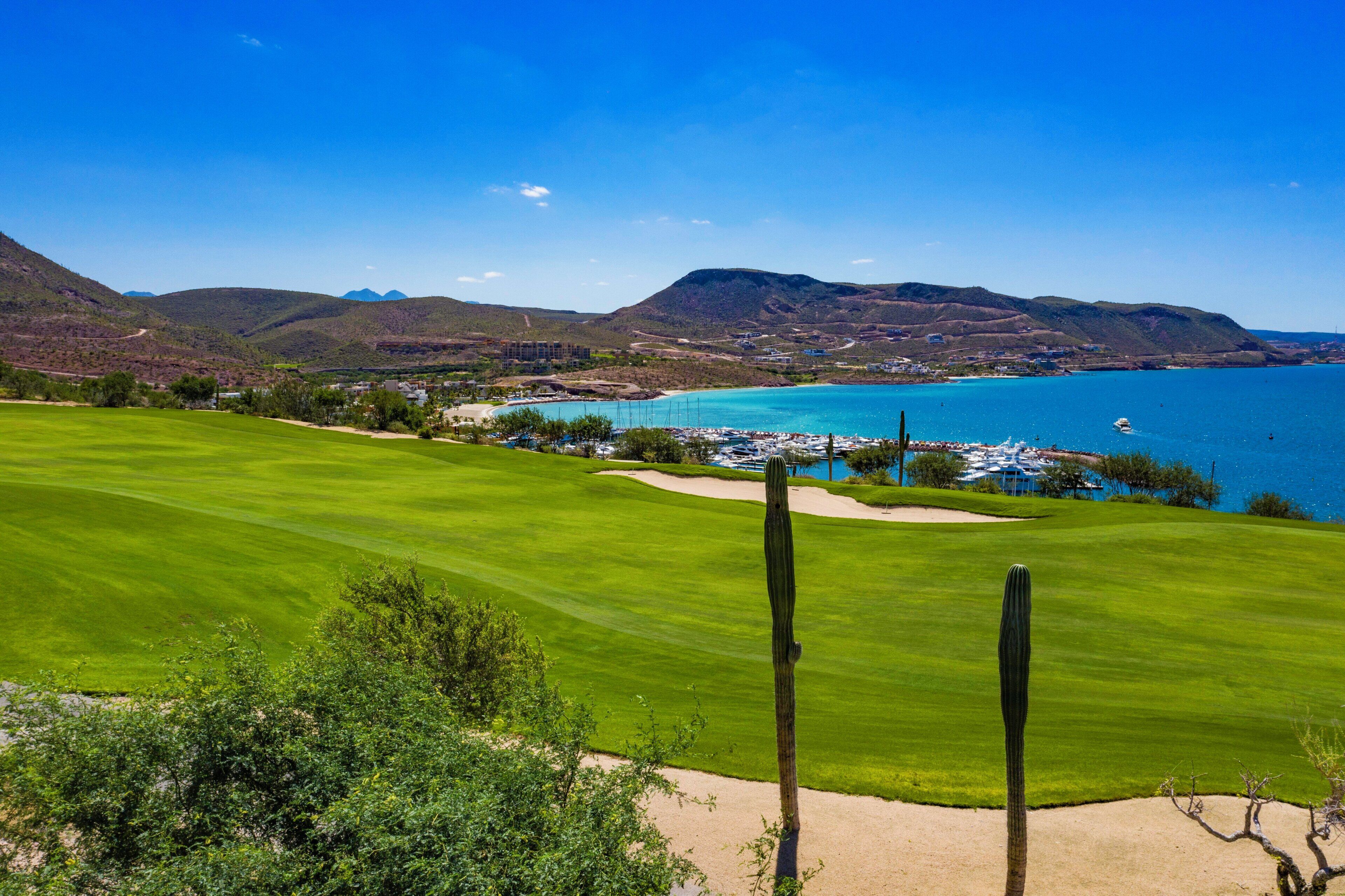 Campo de golf con vistas a un pueblo costero y montañas al fondo.