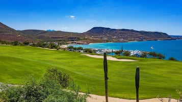Campo de golf con vistas a un pueblo costero y montañas al fondo.