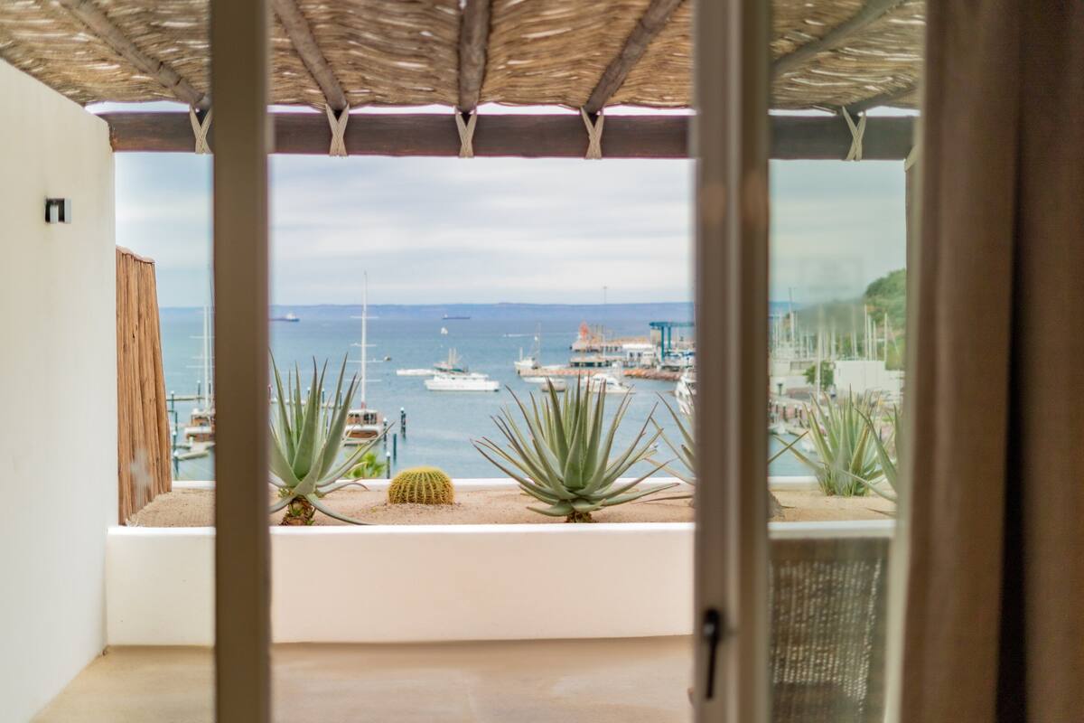 Un balcón con vistas al mar, que incluye un techo de paja y plantas en macetas.