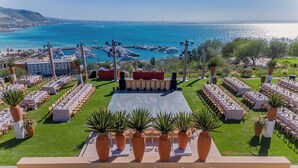 Un espacio al aire libre para eventos, con un escenario, filas de mesas y plantas en macetas.