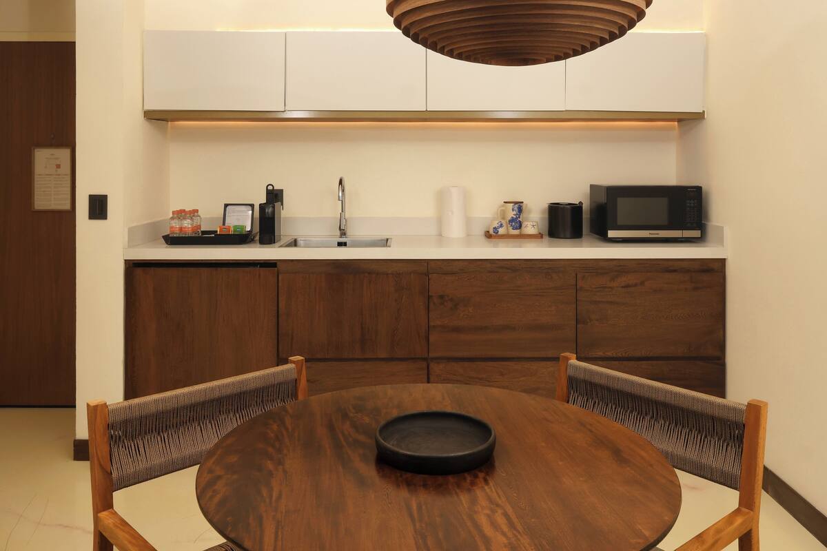Una cocina moderna con microondas, pileta y muebles de madera. Se observa una mesa redonda con dos sillas.