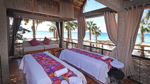 Una habitación con dos camillas de masaje, un sofá con almohadones de colores y vista a la playa.