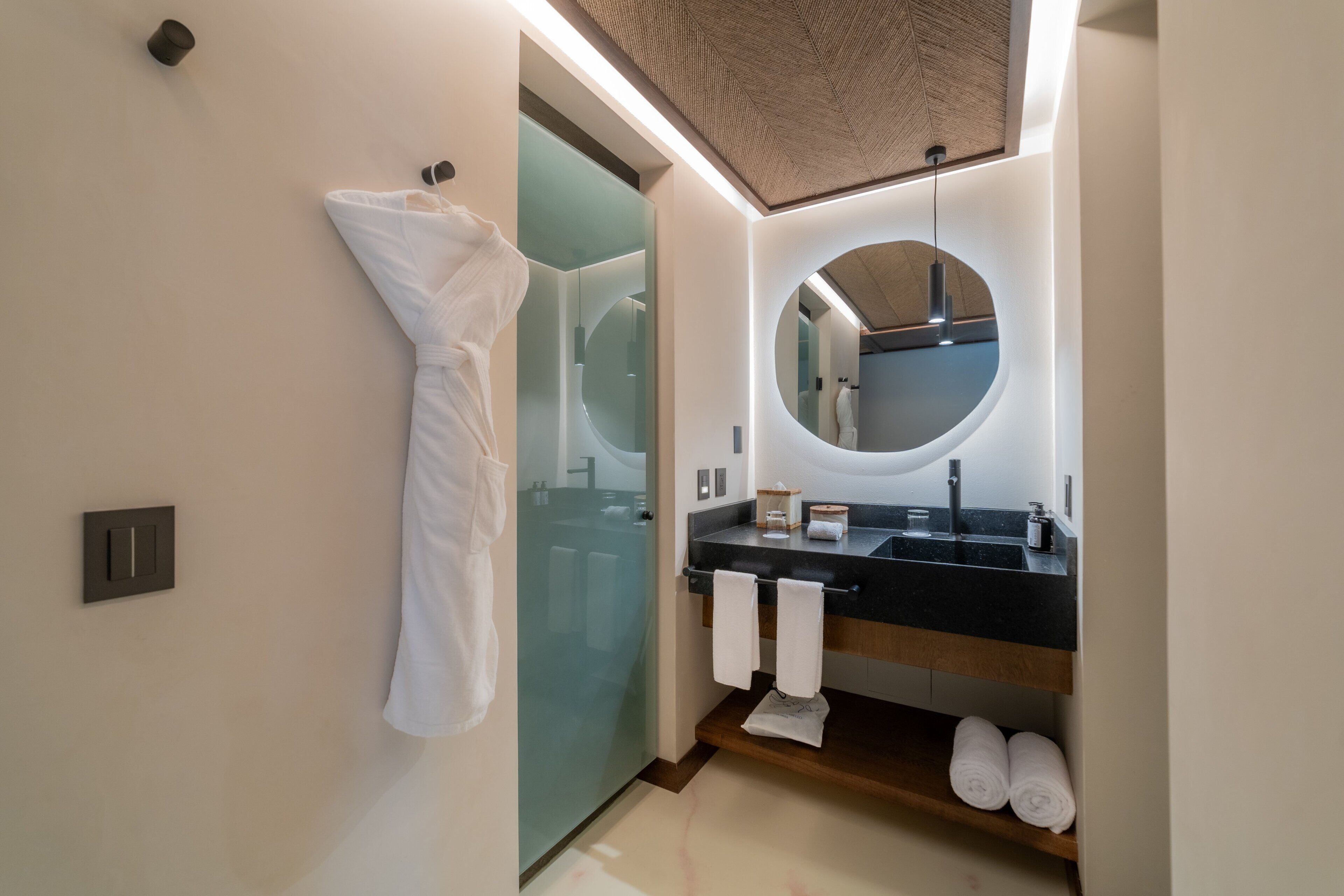 A modern bathroom with a glass shower enclosure, a round mirror, and a black countertop with a sink.
