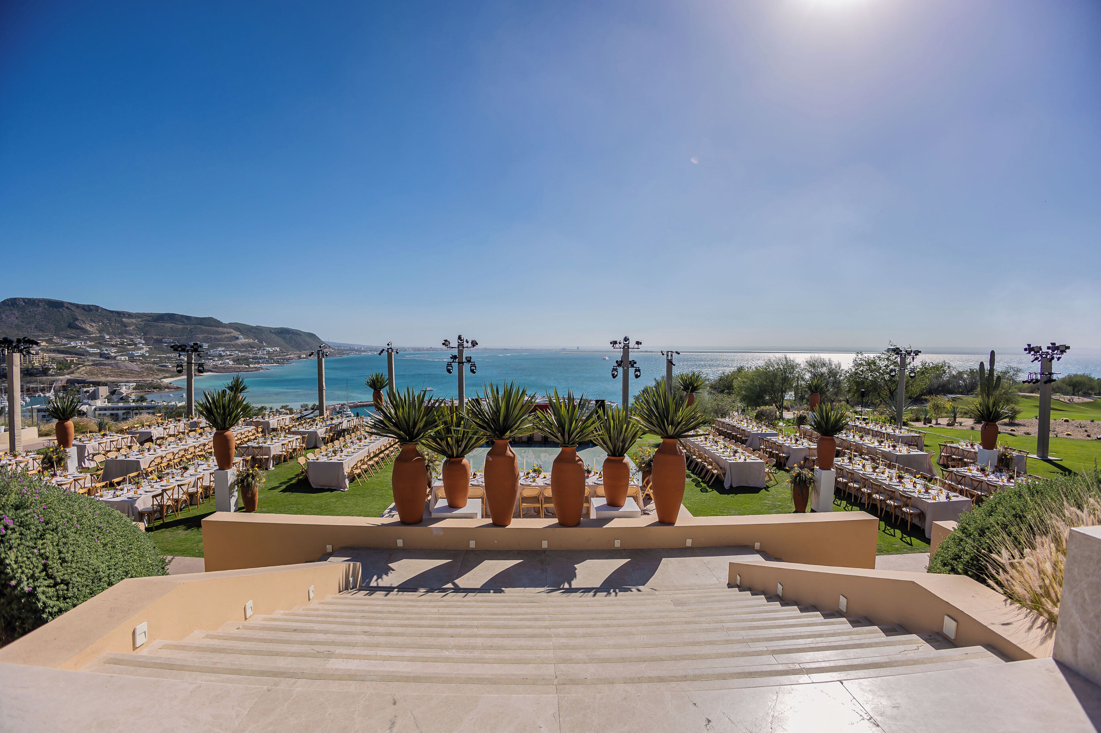 A terrace with outdoor seating overlooking a coastal view, featuring a clear sky and a distant shoreline.