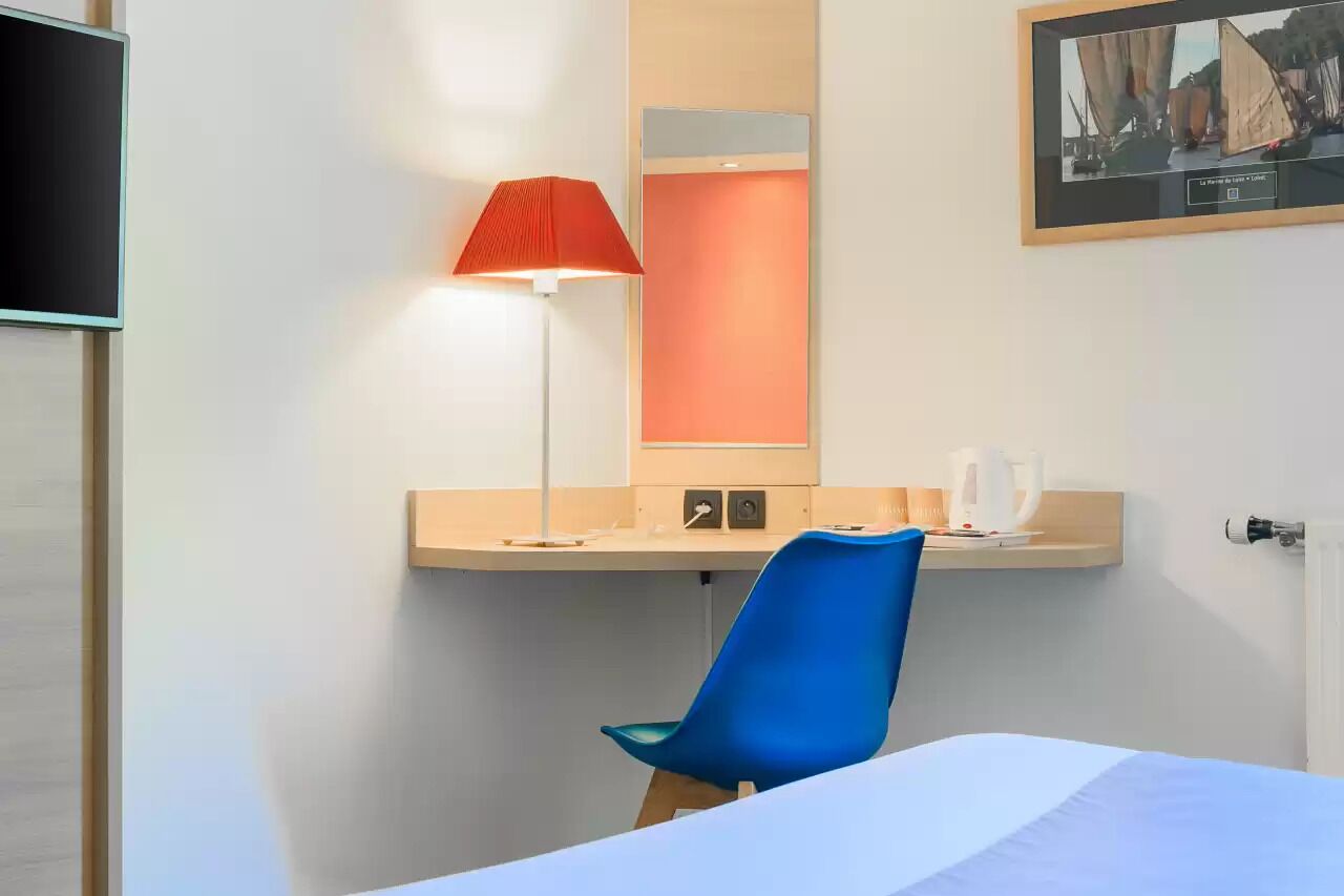 A hotel room with a bed, a desk with a lamp, a chair, and a television.