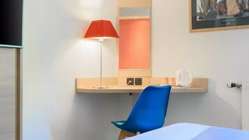 A hotel room with a bed, a desk with a lamp, a chair, and a television.