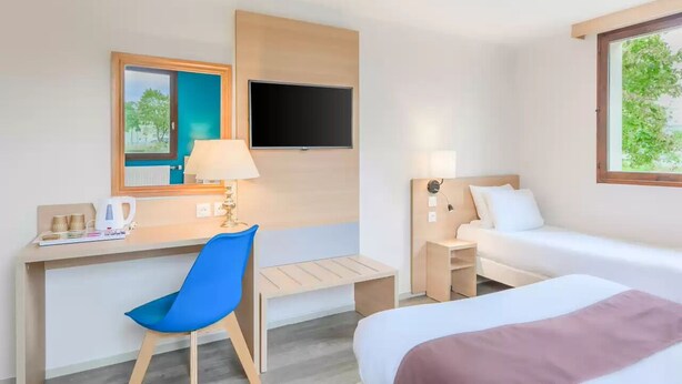 A hotel room with a bed, a desk with a chair, a TV mounted on the wall, and a window with a view of trees. - Comfort Hotel Pithiviers (Pithiviers)