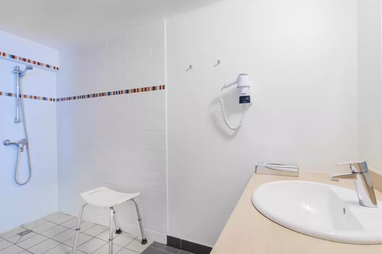 A bathroom with a shower, a white sink, and a small stool.