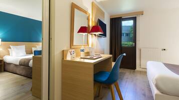 A hotel room with a bed, a desk with a chair, a mirror, a red lamp, and a window with curtains.