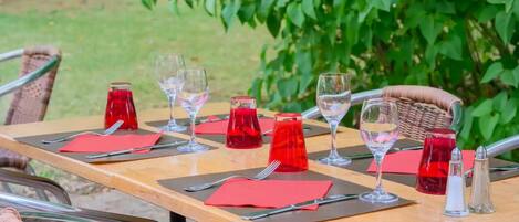 Mesa colocada al aire libre con servilletas rojas, copas de vino transparentes y salero y pimentero.