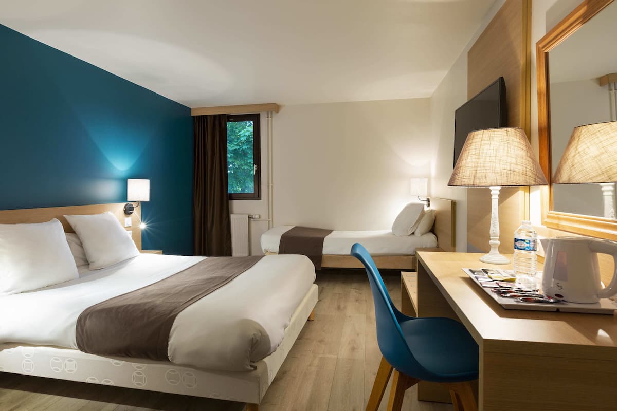 A hotel room with a bed, a desk, a chair, a lamp, a mirror, and a window.