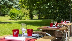 An outdoor dining area with tables set for two, each with a red glass and a white plate. - Comfort Hotel Pithiviers (Pithiviers)