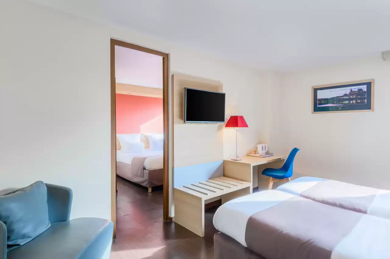 A hotel room with a bed, a desk with a chair, a TV, and a picture on the wall.