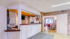 A modern kitchen with white cabinetry and a brick accent wall, leading to a dining area with red chairs. - Comfort Hotel Pithiviers (Pithiviers)