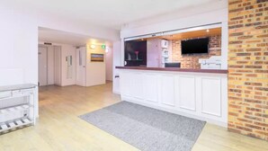 A modern kitchen with white cabinetry, a brick accent wall, and a flat-screen TV mounted above the counter. - Comfort Hotel Pithiviers (Pithiviers)