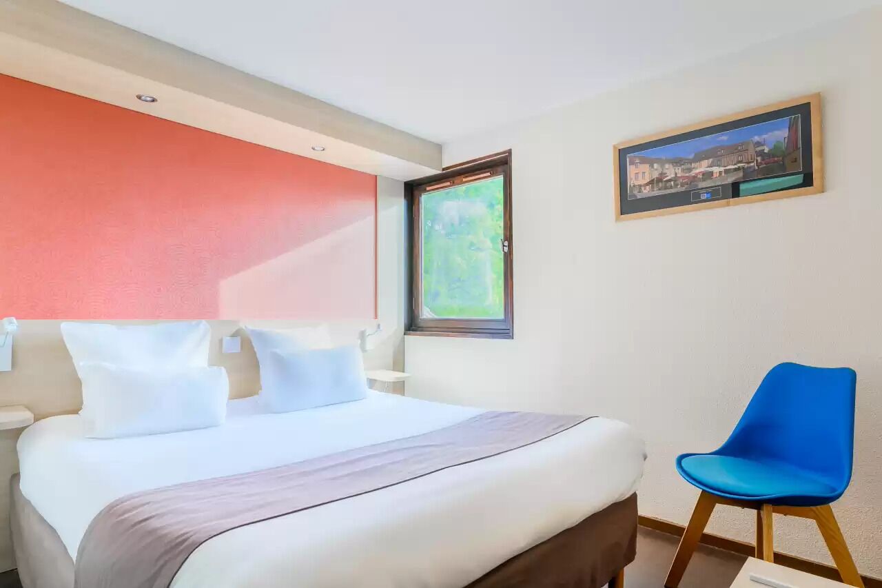 Une chambre d’hôtel avec un lit, une chaise bleue, une fenêtre donnant sur un paysage agréable et un tableau encadré au mur.