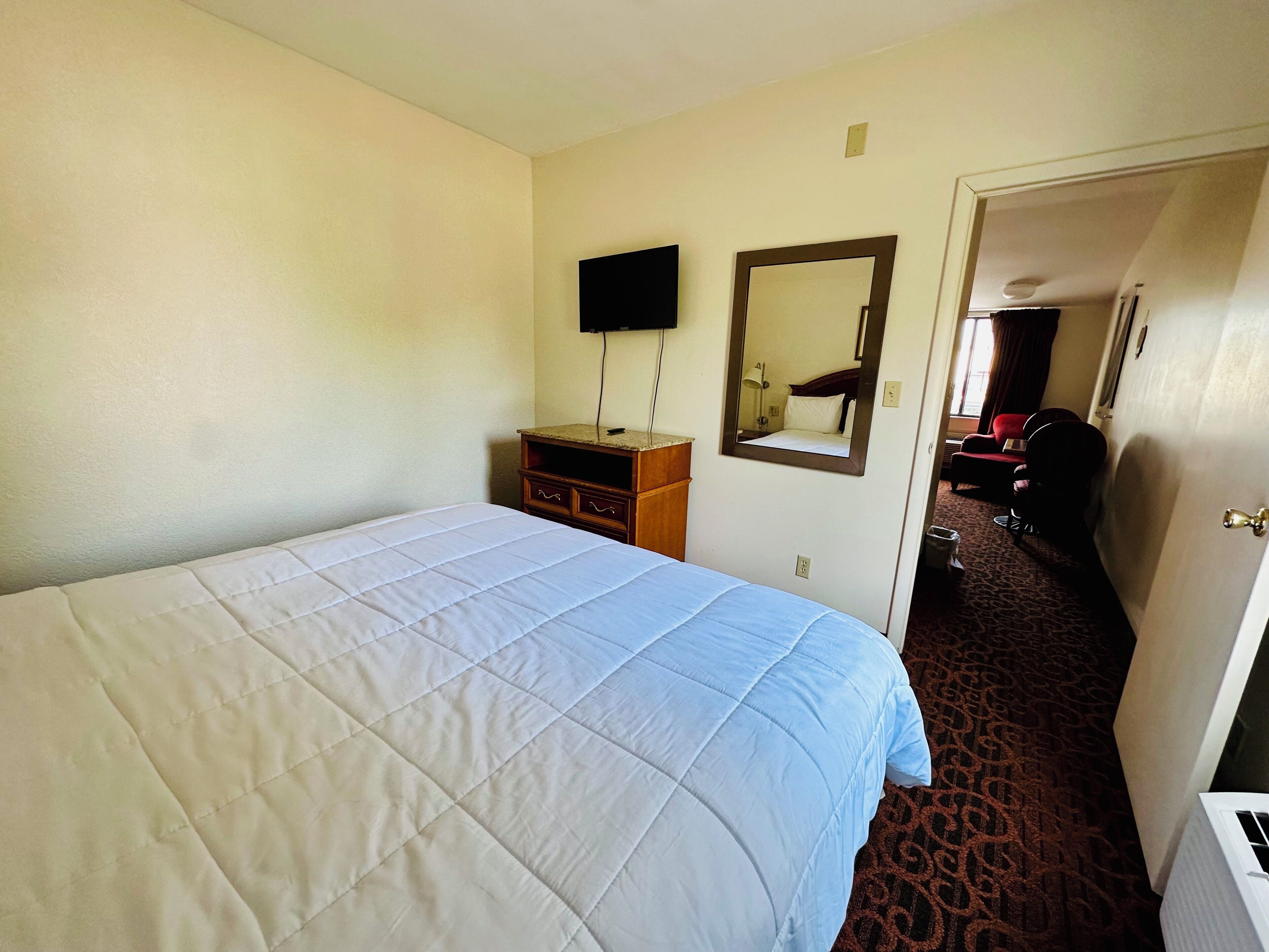 A hotel room with a bed, a dresser, a mirror, and a television on the wall.